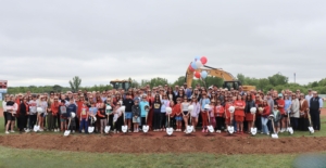 large group photo of children and adults wearing sunglasses with construction equipment in the background